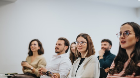 Seitliche Aufnahme von sechs Personen, die in zwei Reihen hintereinander in einem Raum sitzen und alle in dieselbe Richtung blicken