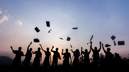 Auf einer Wiese stehen vor einer untergehenden Sonne die Umrisse von mehreren Personen. Die Personen werfen verschiedene Zettel in die Luft