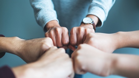 Nahaufnahme der zu Fäusten geballten Hände von drei Personen, die die Hände alle in die Mitte zueinander halten