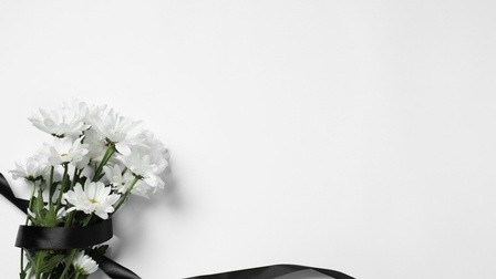 Ein Blumenstrauß, lose umwickelt von einem schwarzen Band, mit weißen Blumen auf weißem Hintergrund in der linken unteren Bildhälfte