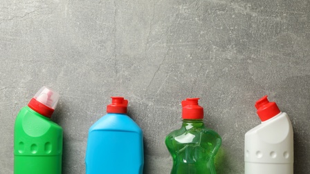 Vier Plastikflaschen mit verschiedenen Putzmitteln vor einer grauen Wand