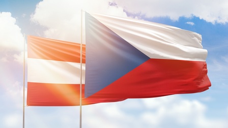 Österreichische Flagge rot-weiß-rot gestreift hinter der tschechischen Flagge, in den Farben blau, weiß und rot. Hinter den Flaggen ist ein Himmel mit Wolken
