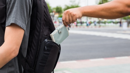 Eine Person stiehlt aus dem Rucksack einer Person eine Geldtasche
