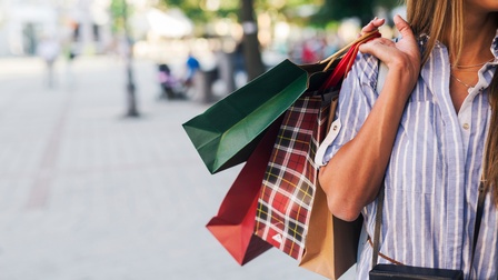 Detailansicht einer Person, die Einkaufstüten mit der Hand über die Schulter trägt