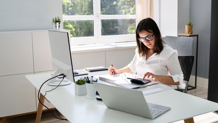 Person mit Brille sitzt an einem Schreibtisch und arbeitet mit einem Laptop