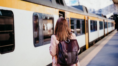 Person in Rückenansicht mit Rucksack steht auf Bahnsteig vor Zug