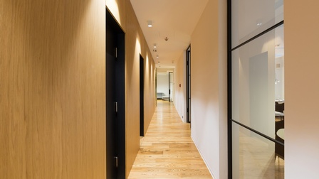Moderne Fluransicht mit Holzboden, weißen Wänden und hellen Glasabschnitten