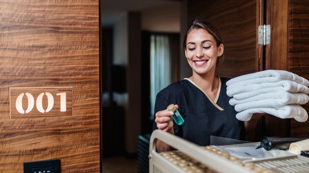 Freudige Person in Arbeitskleidung bei der Reinigung eines Hotelzimmers