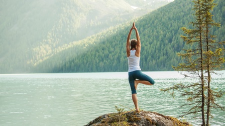 Person in Yogapose vor See mit Waldlandschaft