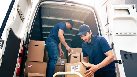 Personen in blauer Arbeitskleidung mit blauer Kappe entladen einen Transporter mit Paketen