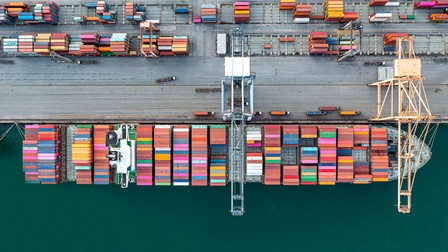 Luftansicht eines beladenen Containerschiffes an Logistikhafen ankernd