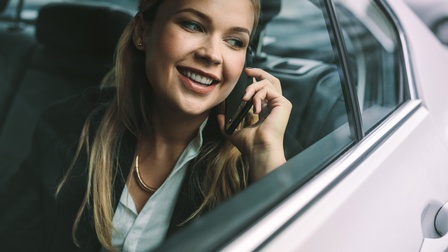 Lächelnde Person auf Autorücksitz sitzend telefoniert