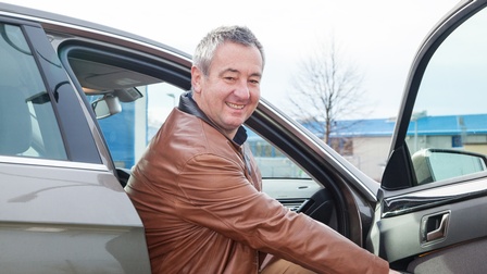 Freudige Person mit Jacke sitzt auf dem Beifahrersitz eines Personenwagens und hält die Autotür offen