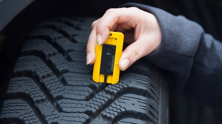 Nahaufnahme Reifenprofil, Hand hält gelbes Messgerät zur Überprüfung
