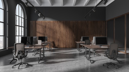 Hoher, großer Raum mit großen Fenstern, in dem Schreibtische, Stühle und Bildschirme stehen