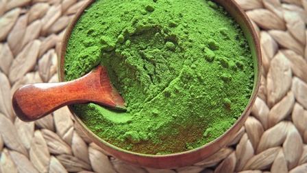 Grünes Matcha Pulver in einer Holzschüssel mit Holzlöffel auf einer geflochtenen Bambusunterlage