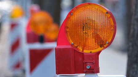 Nahaufnahme einer orangen Warnleuchte an einer Baustelle. Im Hintergrund stehen weitere Warnleuchten