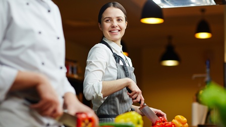 Zwei Personen in Kochmonturen beim Schneiden von Paprikas