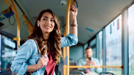 Lächelnde Person steht in einem öffentlichen Bus und hält sich an einer Schlaufe während der Fahrt fest