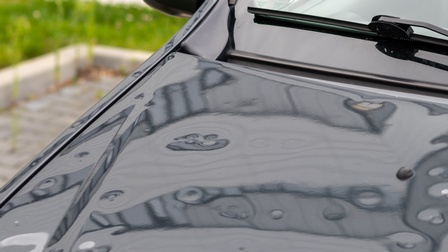 Detailansicht einer Motorhaube eines dunklen Fahrzeugs voller Dellen