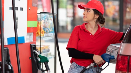 Person in roter Arbeitskleidung tankt ein Auto und blickt dabei auf die Tankanzeige