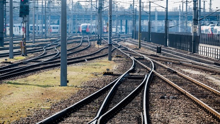 Mehrere leere Bahngleise verlaufen parallel und ineinander. Im Hintergrund stehen Züge.