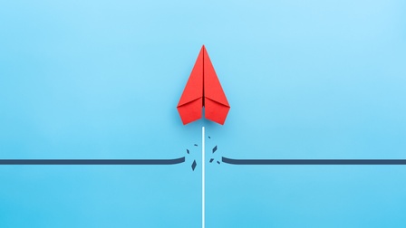 Roter Papierflieger durchbricht eine Linie und startet senkrecht nach oben