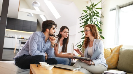Drei Personen sitzen an Couchtisch in Wohnung und unterhalten sich