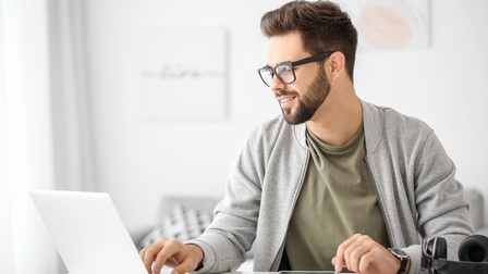 Person mit Brille und Bart blickt auf aufgeklapptes Notebook