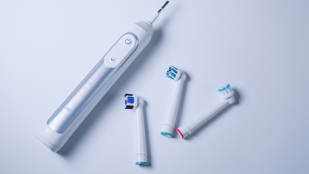 Elektrische Zahnbürste, daneben drei Aufsätze