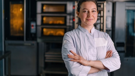 Bäckerin steht mit verschränkten Armen vor dem Backofen
