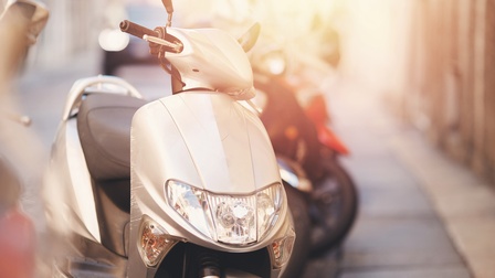 Ein weißer Motorroller von vorne. Im Mittelpunkt befinden sich die Frontverkleidung mit Scheinwerfer sowie der Lenker und der schwarze Sitz. Rechts dahinter steht ein weiterer Motorroller