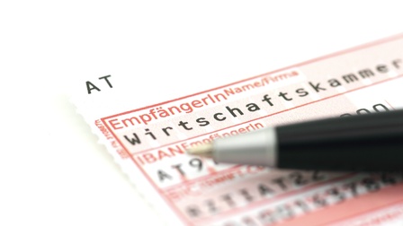 Auf weißem Hintergrund liegt ein Zahlschein. Im Zahlschein ist der EmpfängerIn Name mit Wirtschaftskammer ausgefüllt und darauf liegt ein schwarzer Stift