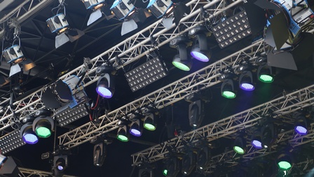 Von der Decke hängen verschiedene, breite Metallkonstruktionen aus Metallstangen. An diesen hängen viele unterschiedliche Scheinwerfer, die in unterschiedliche Richtungen gedreht sind