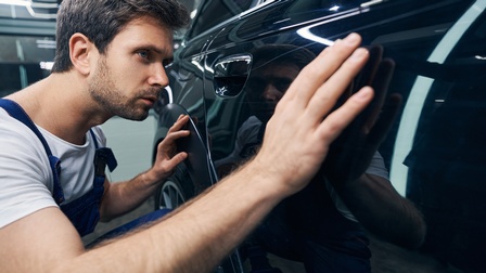 Person inspiziert Autolackierung und streicht mit Hand über Autotür