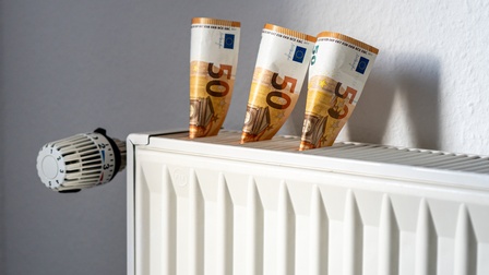 Nahaufnahme von einem weißen Heizkörper mit Thermostat und drei 50-Euro-Scheinen, die aus der Heizöffnung herausstehen, Konzept für Heizkosten Teuerungen 
