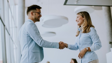 Personen in hellblauer Kleidung stehen in einem Raum und geben sich lächelnd die Hand