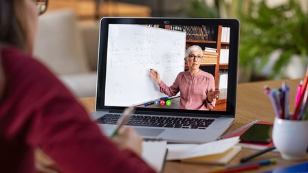 Laptop-Bildschirm mit Person die auf Tafel zeigt, vor Laptop Person sitzend, die Notizen macht