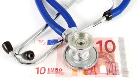 Ein Stethoskop liegt auf einem 10-Euro-Schein auf weißer Oberfläche.
