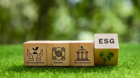 Auf einem grünen Rasen liegen vier Würfel nebeneinander. Auf dem ersten steht environment, auf dem zweiten social, auf dem dritten governance, auf dem vierten esg