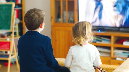Rückenansicht zweier nebeneinander sitzender Kinder, die fernsehen