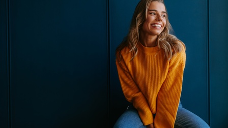 junge Frau in gelbem Pullover vor blauem Hintergrund
