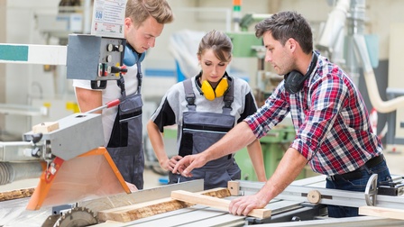 Personen in einer Tischler Werkstätte stehen bei einer Kreissäge