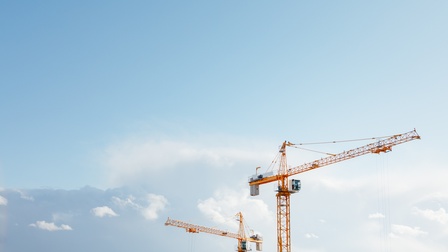 Zwei hohe, gelbe Kräne mit Fahrerkabinen vor blauem Himmel