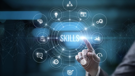 Hand einer Person in Businesskleidung zeigt mit einem Finger auf Grafik mit Schriftzug Skills als Konzept von Fähigkeiten, daneben sind mehrere Icons zum Thema kreisförmig vor einem dunklen Hintergrund angeordnet