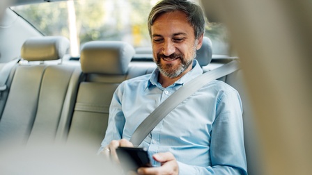 Lächelnde Person auf Autorücksitz blickt auf Smartphone