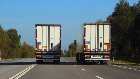 Rückansicht von zwei LKWs, die auf einer Straße nebeneinander fahren und TIR-Schild montiert haben