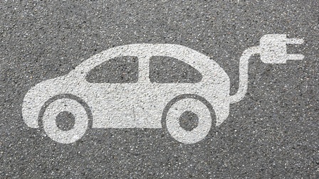 Auf asphaltiertem Untergrund ist das Symbol eines weißen Autos mit einem Stecker aus dem Kofferraum ragend.