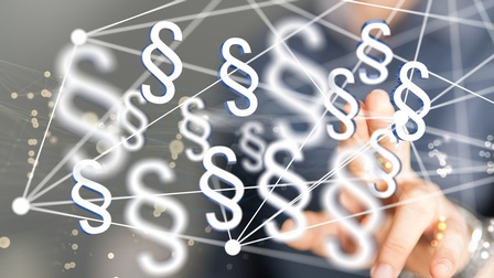 Nahaufnahme einer Person, die mit dem linken Zeigefinger auf eine Scheibe tippt. Auf der Scheibe sind weiße Symbole von Paragraphen, sowie Linien, die von weißen Punkten ausgehen. Im Hintergrund sind gelbe Punkte