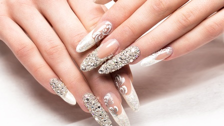 Nahaufnahme von langen Fingernägeln mit glitzernden Strasssteinen.